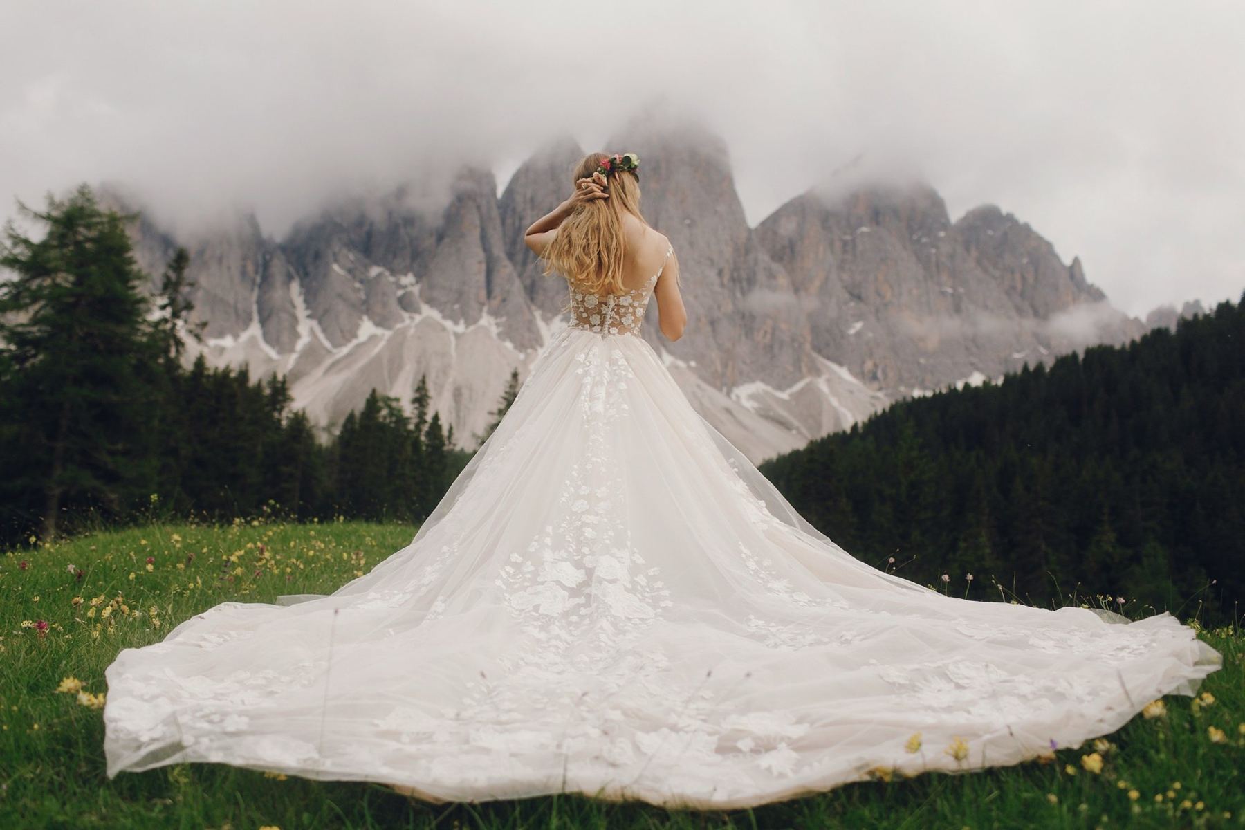 A bride in a mountain meadow, her gown spread across the grass