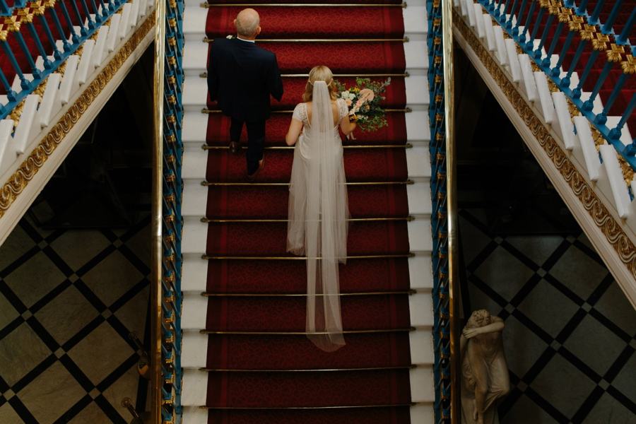 A bride walking up a red-carpeted staircase, filmed from above